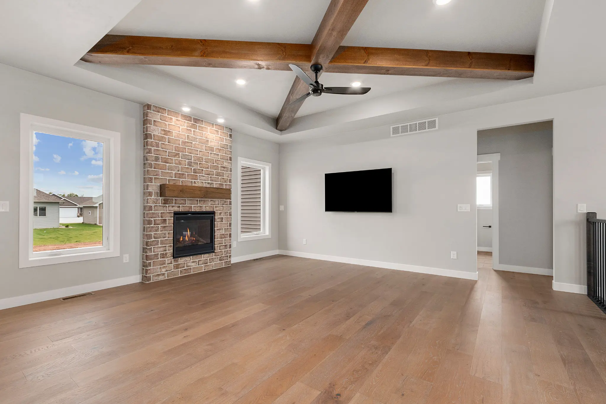Riverwood living room with wood ceiling beams, a brick fireplace, and wide-plank flooring
